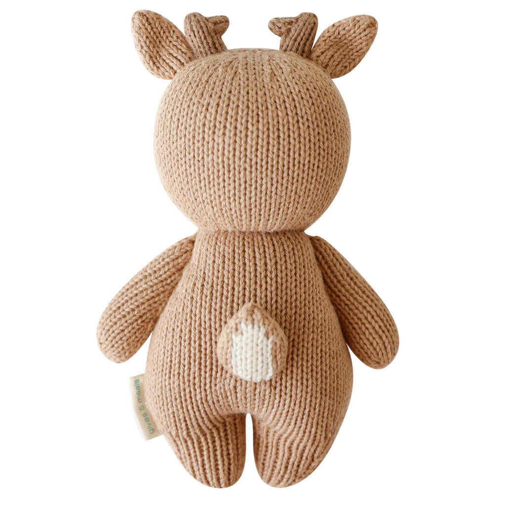 A hand-knit Cuddle + Kind Baby Fawn with white details on its belly and inner ears, featuring small antlers and a tail, standing upright against a white background.