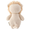 A soft, beige hand-knit Cuddle + Kind Baby Lion with a fluffy head and no facial features, lying on its back with a visible label tag on the side.