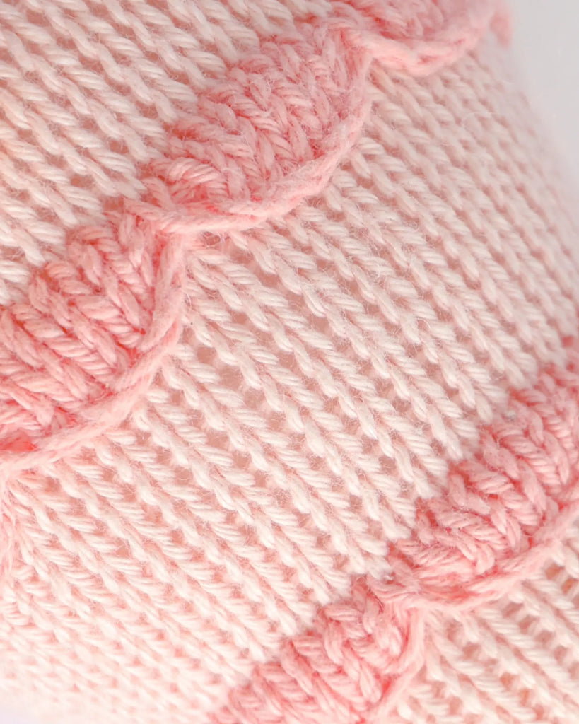 Close-up of pink and cream knitted fabric with wavy stripes, soft yarn, and visible stitches—reminiscent of the charm found in Cuddle + Kind Baby Fish.