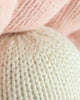 Close-up of Cuddle + Kind Baby Pearl shows soft, heirloom-quality knitted fabric in pale pink and off-white, highlighting the texture and pattern of natural cotton yarn.