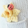 Close-up of Cuddle + Kind Beatrice The Mouse - Periwinkle, featuring a knitted yellow flower with a small red and black ladybug on light gray fabric; handmade with sustainable fair trade practices.