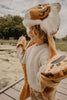 A child beams in the Costume - Tiger, a cozy faux fur outfit with a tiger-face hood and matching mittens, standing on a wooden dock by a tree-lined lake.