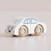 A small white wooden toy car with black details and wooden wheels sits on a light surface. The car, the No. 20 GT110 Rene made in England, is a classic toy designed for imaginative play, featuring simple painted windows and door outlines, with “LETOVIAN” written on the wheels.