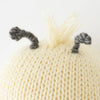 Close-up of a Cuddle + Kind Baby Bee hand-knit hat with fluffy white and gray pom-pom details resembling ears, against a white background.