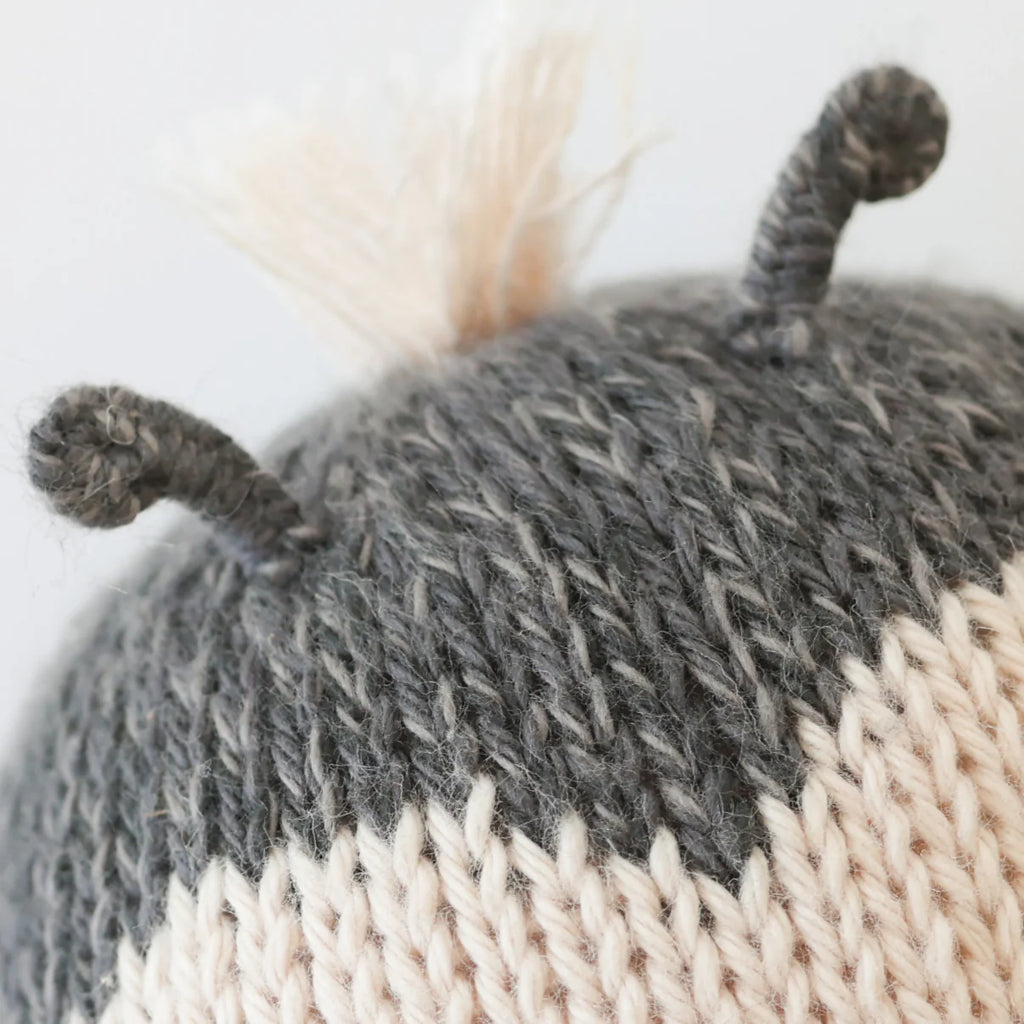 Close-up of the Cuddle + Kind Baby Ladybug, hand-knit in gray and cream Peruvian cotton, featuring two small curved gray antennae and a tuft of cream yarn on top.