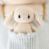 Cuddle + Kind Briar the Bunny – Light Blue is a small, cream-colored hand-knit doll with long ears, nestled in the front pocket of a light blue cotton yarn garment.