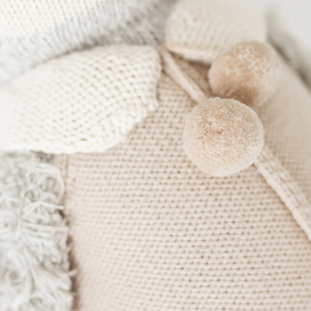 Close-up of Cuddle + Kind Greyson the Penguin, a cotton yarn doll in soft beige and cream with textured details, two fluffy pom-pom buttons, and a ribbed collar, showcasing a cozy handmade look.