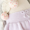 Close-up of Cuddle + Kind Skylar The Penguin, a fair trade knit cotton doll dressed in a pastel lilac skirt with a bow at the waistband, cream top, and soft pink and white pom-pom decorations.