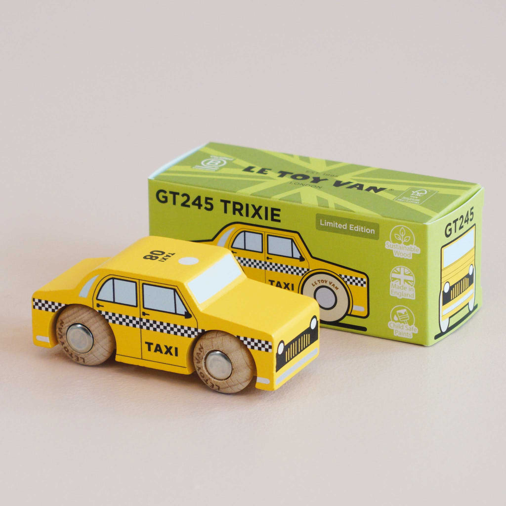 A yellow wooden taxi labeled “TAXI” sits in front of a green box that reads “No. 39 GT245 Trixie | Made in England.” Designed to spark imaginative play, this wooden taxi and its box both feature classic black checkered detailing reminiscent of a New York taxi.