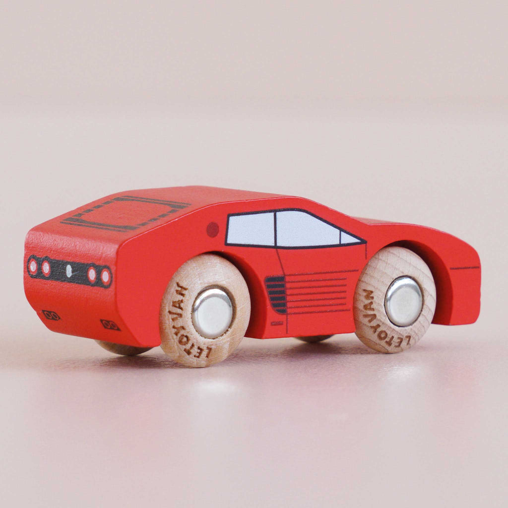 A small red wooden racing car, No. 25 GT140 Marco made in England, featuring white wheels, black accents, and minimalist printed windows, viewed from the rear against a light background.