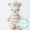 A hand holding a small, hand-knit stuffed animal resembling a Cuddle + Kind Baby Zebra, with a badge on the image stating "best toy 2022 good housekeeping awards." The background is plain white.