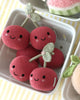 Six Cuddle + Kind Baby Cherries, each with a smiling face and leaf-topped stem, are arranged in a white dish for an adorable and whimsical display. Handcrafted from natural Peruvian cotton yarn, these cherries offer heirloom quality that blends charm with lasting durability.