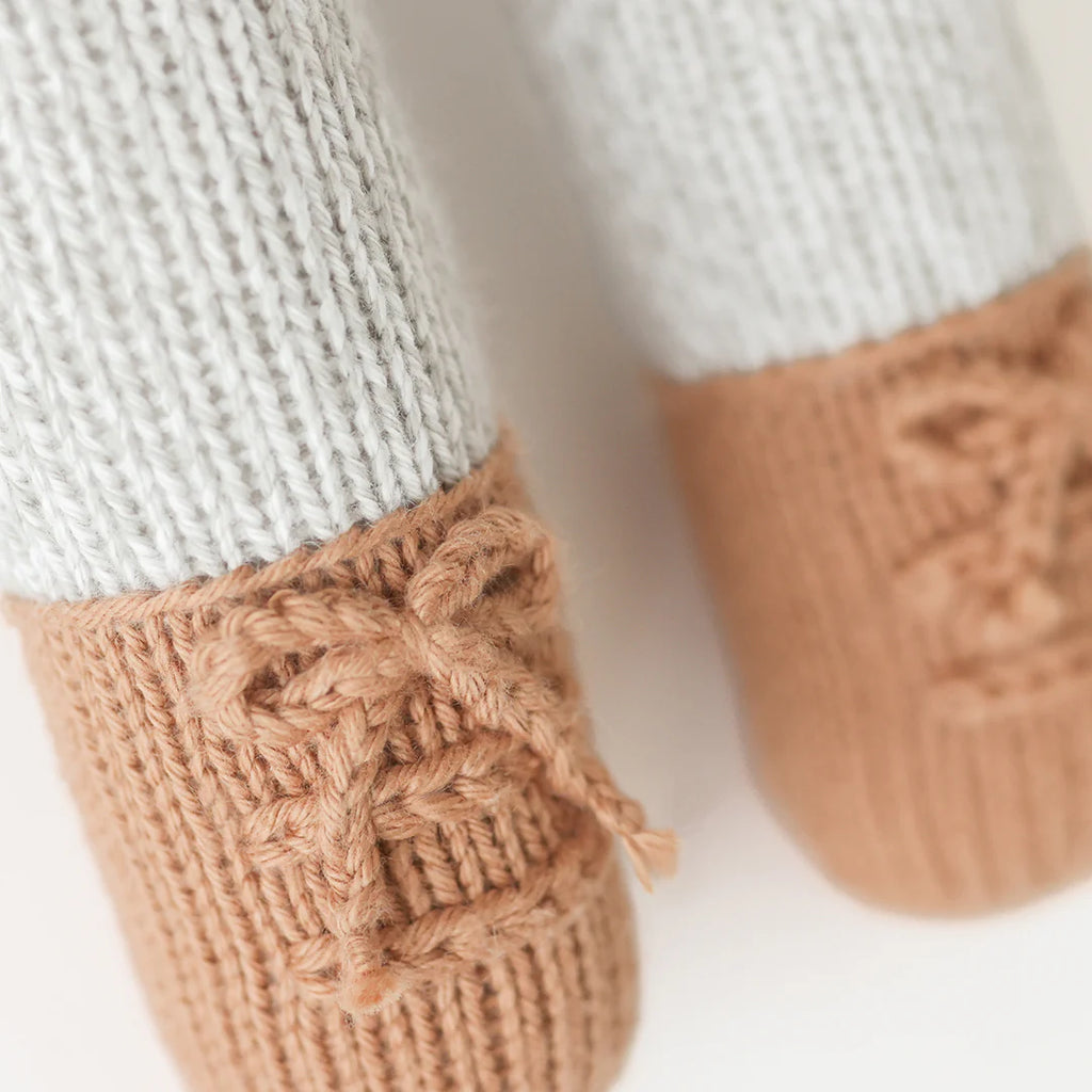 Close-up of Cuddle + Kind Greyson the Penguin’s cream knitted legs with brown yarn shoes and crocheted laces, part of this hand-knit fair trade stuffed animal.