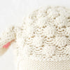 Close-up of Cuddle + Kind Avery the Lamb’s cream-colored, 100% cotton yarn fabric, featuring a soft, bumpy knit texture and a cozy look. Part of the hand-knit doll's fabric is tied in a knot to the left.