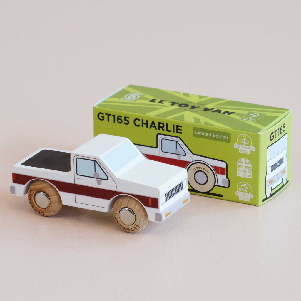 A classic toy truck, the No. 30 GT165 Charlie | Made in England wooden pick-up truck with a red stripe sits in front of its green and yellow box, which is labeled “GT165 CHARLIE Limited Edition” and features an illustration of the off-road vehicle toy.