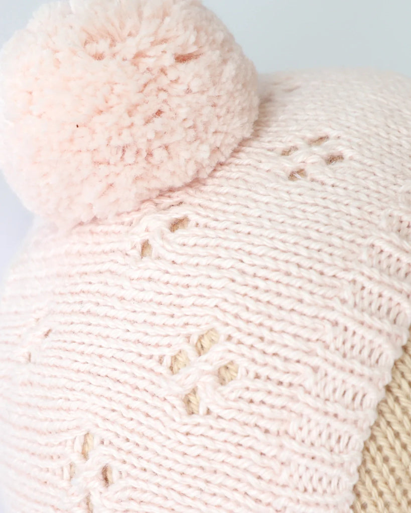 Close-up of the Cuddle + Kind My First Baby (Blush) hat, featuring light pink hand-knit cotton with a large pom-pom, ribbed edge, and openwork diamond pattern. Ships in one week.