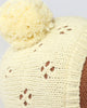 Close-up of the Cuddle + Kind My First Baby (Buttercup), a hand-crafted, cream-colored knitted hat made from natural cotton yarn with delicate patterns and a large fluffy pom-pom. Ships in one week.