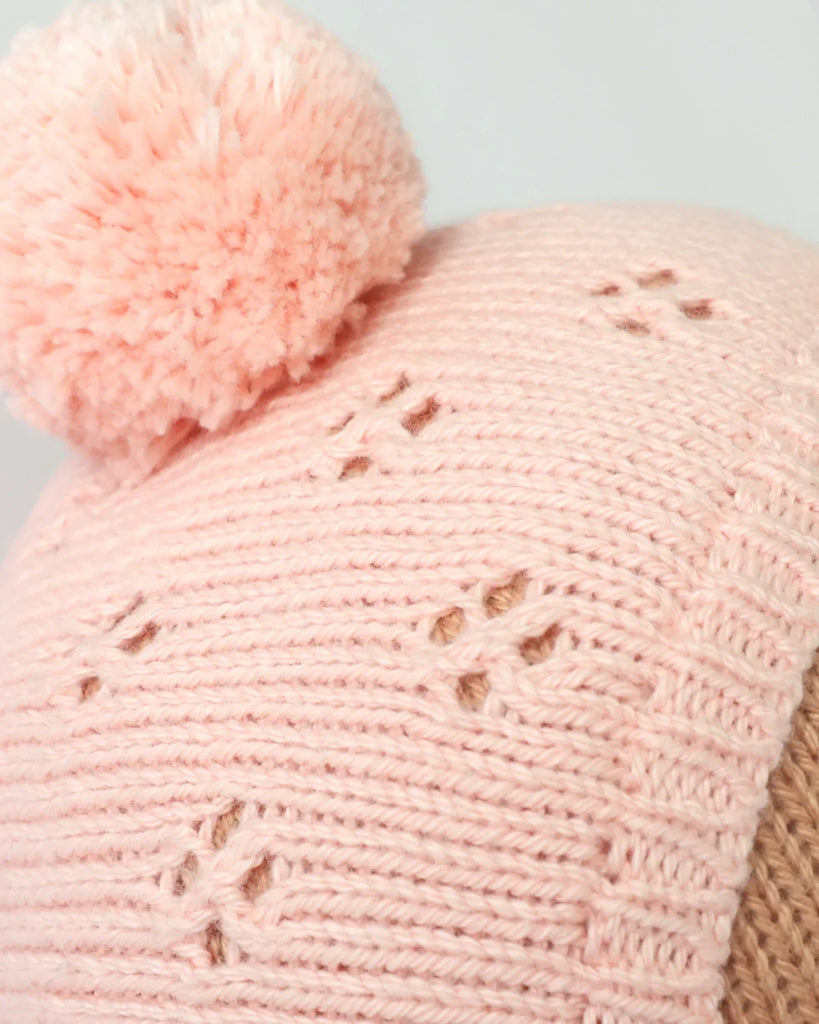 Close-up of the Cuddle + Kind My First Baby (Peach) hat, a hand-knit, light pink baby doll accessory with a fluffy pompom, made from natural cotton yarn and delicate decorative holes. Ships in one week.