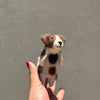 A hand with red nail polish displays the Felt Finger Puppet: Jack Russell Terrier Dog, made of wool felt, against a plain light gray background.