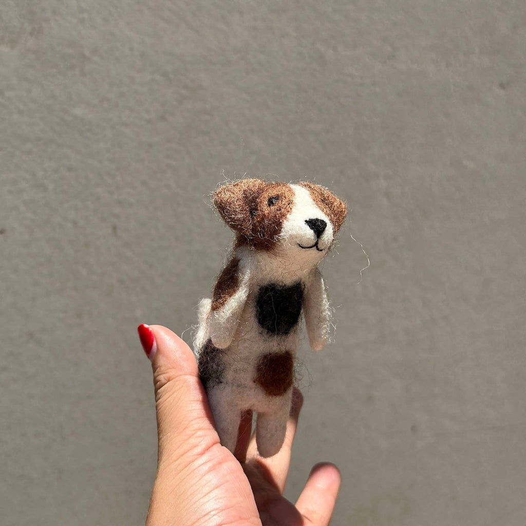 A hand with red nail polish displays the Felt Finger Puppet: Jack Russell Terrier Dog, made of wool felt, against a plain light gray background.