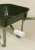 Close-up of the Heritage Wheelbarrow – Liane, a green children's wheelbarrow with a white ribbed handle and part of the frame visible, set against a beige background. "COCO VILLAGE" is printed on the side, making it a charming kids' garden tool.