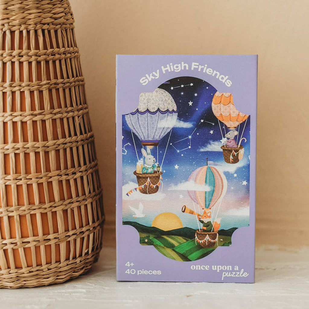 A whimsical 40-piece puzzle, “Sky High Friends 40 Piece Mini,” comes in a purple box featuring animals riding in hot air balloons across a starry sky above a colorful landscape. The packaging reads “Sky High Friends,” “once upon a puzzle,” is suitable for ages 4 and up, and sits next to a charming wicker basket—making it the perfect choice to spark young imaginations.
