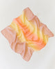 A charming, soft square silk scarf named Sarah's Silk Enchanted Playsilk - Desert features a pastel gradient of pink, yellow, and orange hues as it lies casually on a plain white background. Resembling playsilks, the fabric invites imaginative play with its smooth yet slightly crinkled appearance.