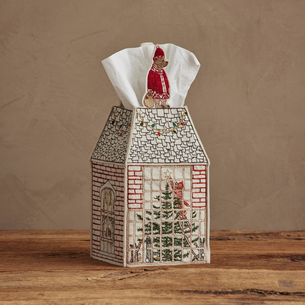 The Coral & Tusk Home for the Holidays Tissue Box Cover is a charming embroidered house-shaped cover featuring festive holiday designs, including a tree in the window and Santa on the roof, perfect for seasonal decor.