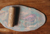 The Flower Roller - Eco Pattern Playdough Roller features delicate floral engravings and rests on marbled pastel clay, leaving beautiful flower imprints on a wooden surface—making it an ideal choice for sensory play and creative fun.