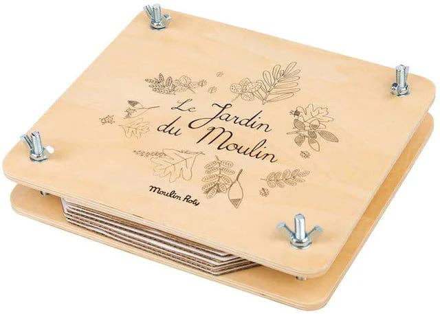 The Moulin Roty Botanist Suitcase is a wooden flower press with metal bolts at each corner, featuring floral illustrations and "Le Jardin du Moulin" in cursive—a charming nature kit for curious minds.
