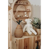 A cozy wooden shelf displays a wicker basket, a Senger Naturwelt Stuffed Animal - White Bear, a potted plant, and a circular wall shelf with wooden toys, blocks, and a small figurine in a softly lit minimalist kids’ room.