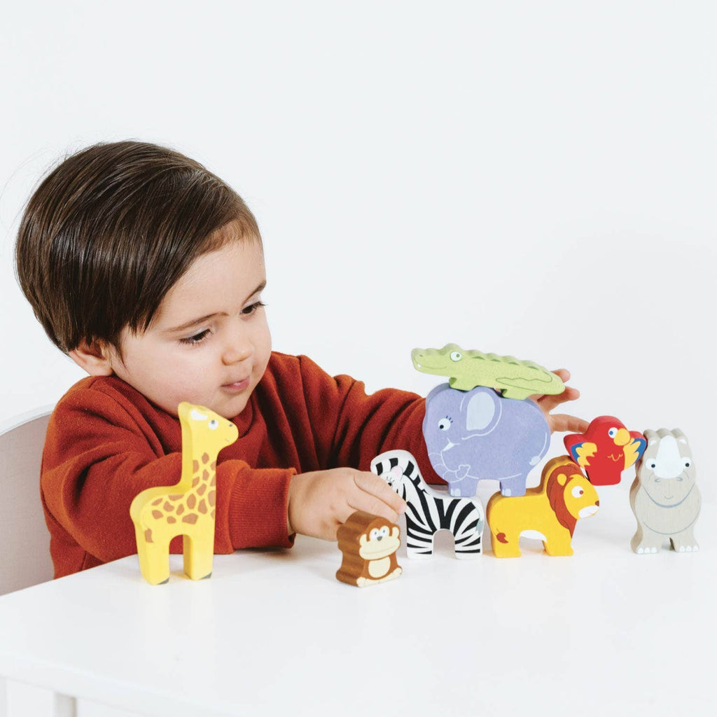 A young child in a red sweater sits at a white table, playing with the Africa Stacking Animals & Bag—a sustainable wooden toy with colorful animal figurines that helps develop fine motor skills.