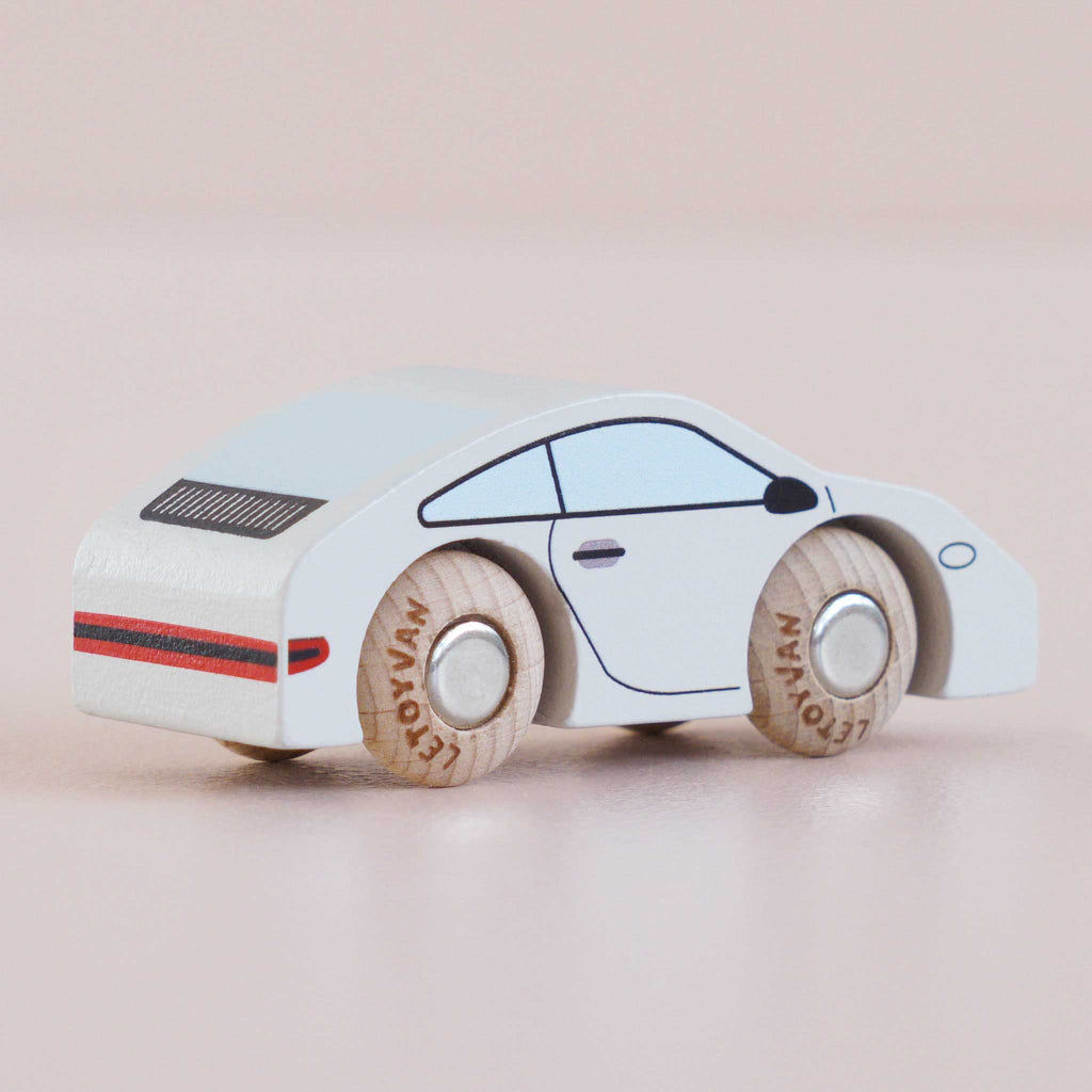 A small white wooden sports car with black and red details and light brown wheels, the No. 16 GT90 Poppy is set against a plain light pink background. This classic toy car is made in the United Kingdom.