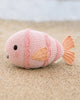 The Cuddle + Kind Baby Fish is a hand-knit pink plush toy with orange fins and tail, black eyes, and a small smile—perfect for cuddling and collecting.