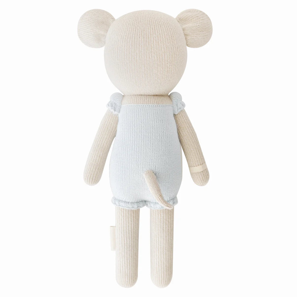 Cuddle + Kind Beatrice The Mouse - Periwinkle is a handmade beige knit stuffed animal with round ears in light blue overalls, crafted from sustainable fair trade materials and hypoallergenic polyfill. The back view shows its tail and arms.