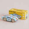 A small blue wooden racing car with the number 6 sits in front of a yellow box labeled “No. 26 GT145 Fred | Made in England,” which features an illustration matching the classic toy car.