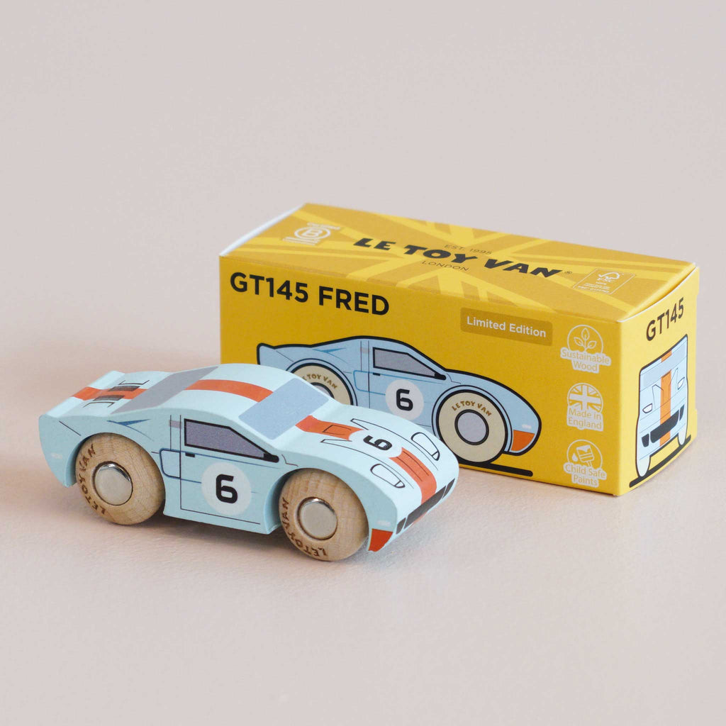 A small blue wooden racing car with the number 6 sits in front of a yellow box labeled “No. 26 GT145 Fred | Made in England,” which features an illustration matching the classic toy car.