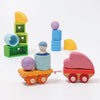 Grimm's Wooden Train Building Set features colorful wooden wagons carrying pastel heart and sphere shapes, with stacked blocks in the background—perfect for inspiring imaginative travel stories on a white surface.