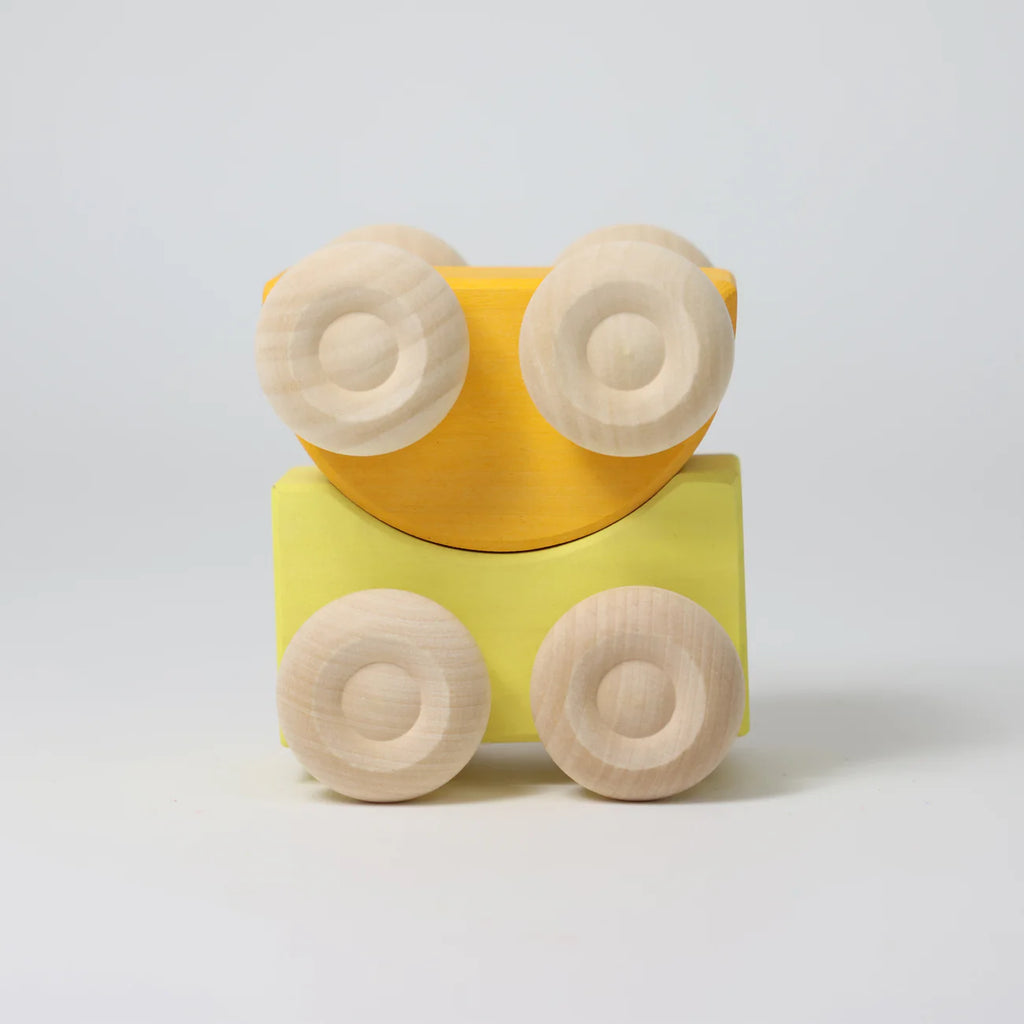 A Grimm's Stacking Cars - Yellow toy, featuring a yellow wooden body and four light-colored round wheels, is displayed against a plain white background.