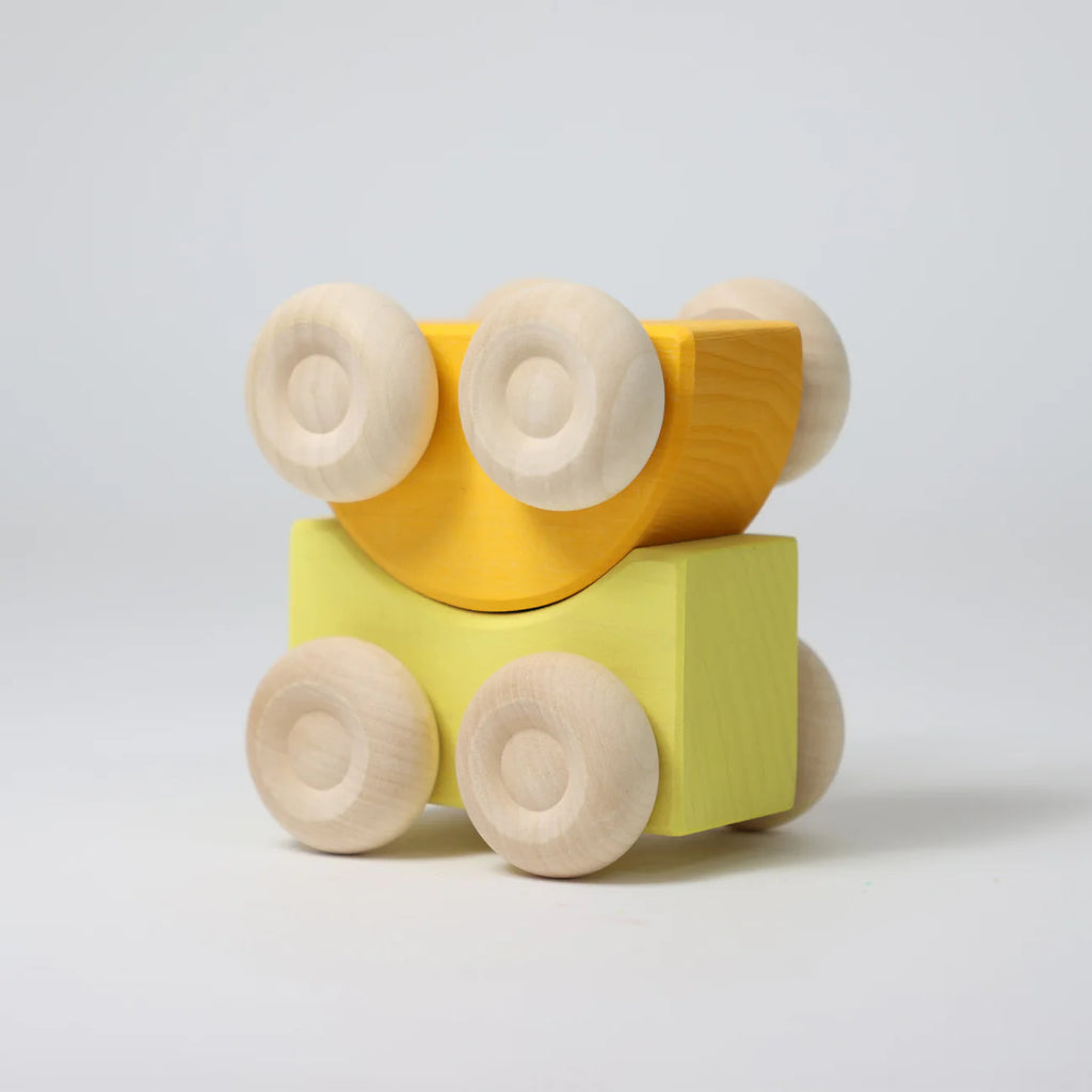 Two Grimm's Stacking Cars - Yellow, one curved yellow and one square light green, are stacked against a plain white background. Both toy cars have round, unfinished wooden wheels.