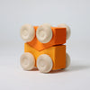 Two orange Grimm’s Stacking Cars - Orange (coming soon), each with four round, light wooden wheels, are stacked together against a plain background. The top block is rectangular and the bottom V-shaped—classic German design.