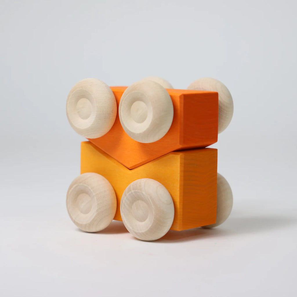 Two orange Grimm’s Stacking Cars - Orange (coming soon), each with four round, light wooden wheels, are stacked together against a plain background. The top block is rectangular and the bottom V-shaped—classic German design.