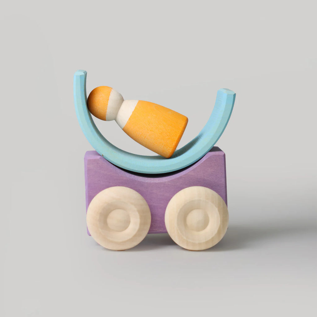 Grimm's Stacking Cars - Purple (coming soon): A minimalist wooden stacking toy with a purple rectangular base on two wheels, a blue semicircular cradle, and a yellow and white figure inside, set against a plain gray background.