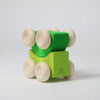 Grimm's Stacking Cars - Green (coming soon) features a green wooden car with six natural wood wheels in two stackable layers, set on a plain white background. The bottom block displays the engraved "Grimm's" logo.