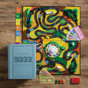 Board Game: The Game of Life Vintage Bookshelf Edition is displayed on a wooden floor with vibrant winding paths, cards, play money, cars, pegs, a spinner, and its signature blue book-style box to the left.