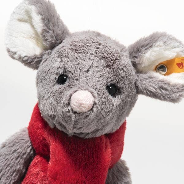 A close-up of the Steiff Cozy Christmas Mia Mouse plush, featuring large ears, black eyes, a pink nose, red scarf, soft fluffy fur, and a small yellow tag on one ear.
