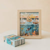 The Ocean Explorers 40 Piece Mini puzzle is shown completed and framed, featuring sailboats gliding on the water as well as a diver, colorful fish, and an octopus beneath the waves. Its matching puzzle box sits beside the frame on a white surface against a beige background—perfect for providing kids with hours of creative jigsaw fun.