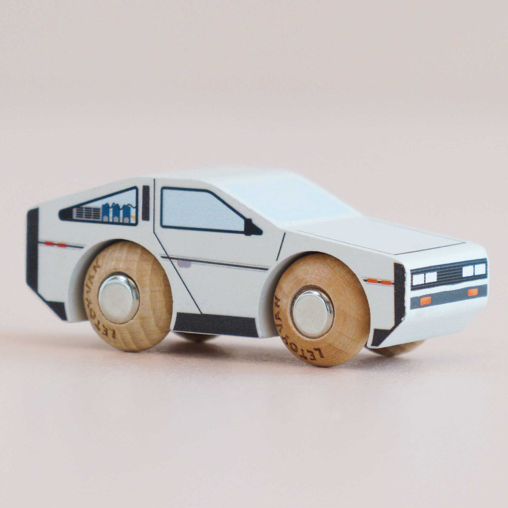 No. 23 GT130 Dexter is a small wooden toy car, painted white with black windows and details to resemble a classic DeLorean. Featuring simple round wooden wheels, this modern toy car is perfect for imaginative play and is set against a light background. Available for pre-order in August 2026.