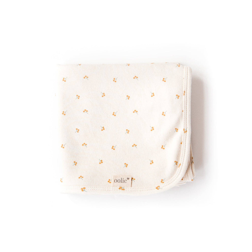 The Organic Baby Blanket – Gold Sprig features a folded, cream-colored design with small yellow floral patterns and an “oolie” label in the corner, crafted from GOTS-certified organic cotton and pictured on a white background.