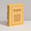 A yellow, book-shaped box of Board Game: Boggle Vintage Bookshelf Edition stands upright on a white surface, showing the classic word game grid and labeling it for ages 8+ and two or more players.